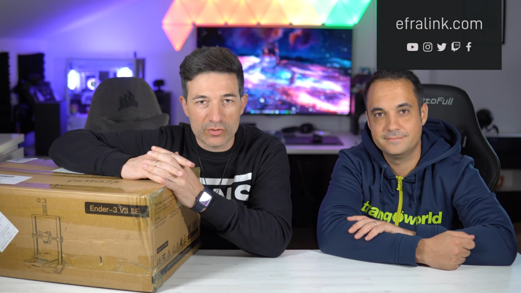 Se ve a Efralink y su amigo Angel sentados frente a una mesa. Sobre la mesa blanca se encuentra la caja de la impresora Creality Ender-3 V3