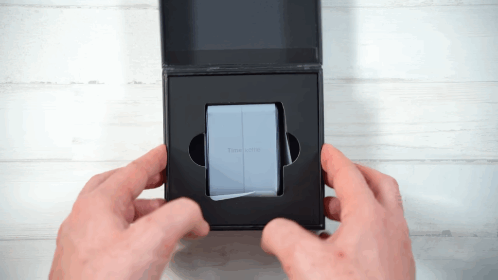 Se ven las manos de Efralink sujetando la caja de los Timekittle W4 con el estuche de carga dentro cubierto con el plástico protector
