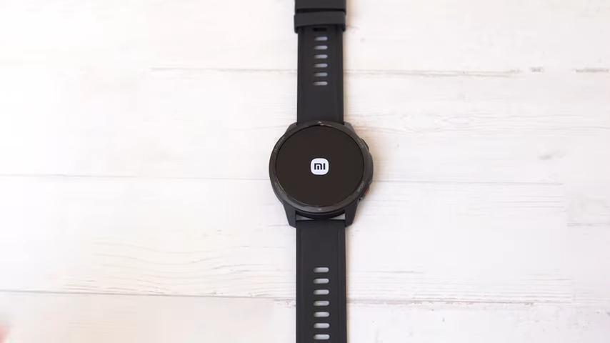 Se muestra el reloj S1 active de Xiaomi sobre una mesa blanca, con la pantalla negra y el logo de xiaomi en medio blanco